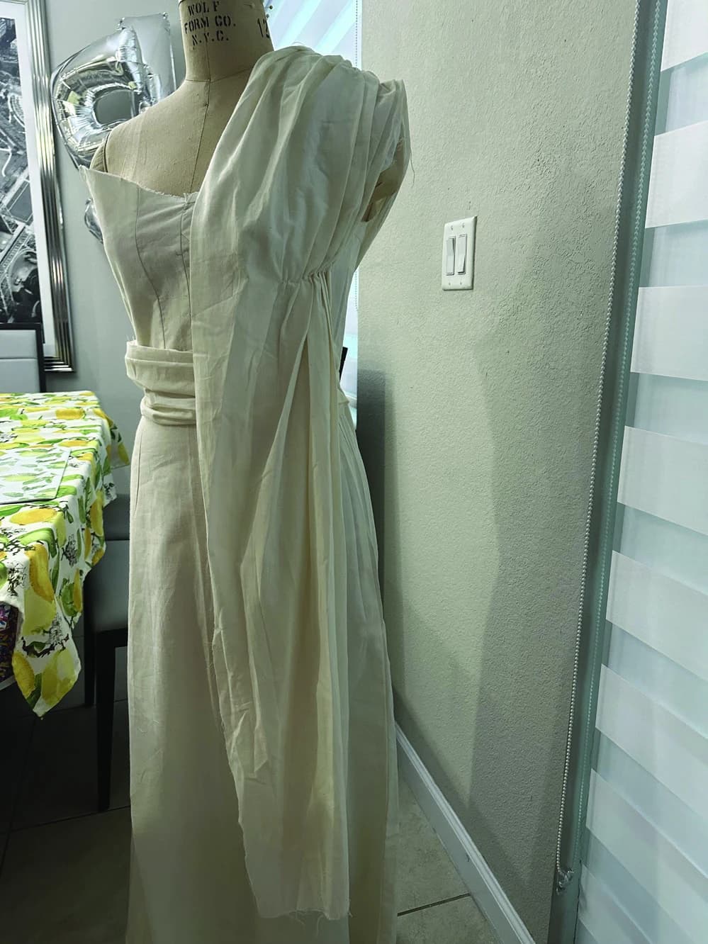 White draped Faith garment in progress on a dress form, side view.